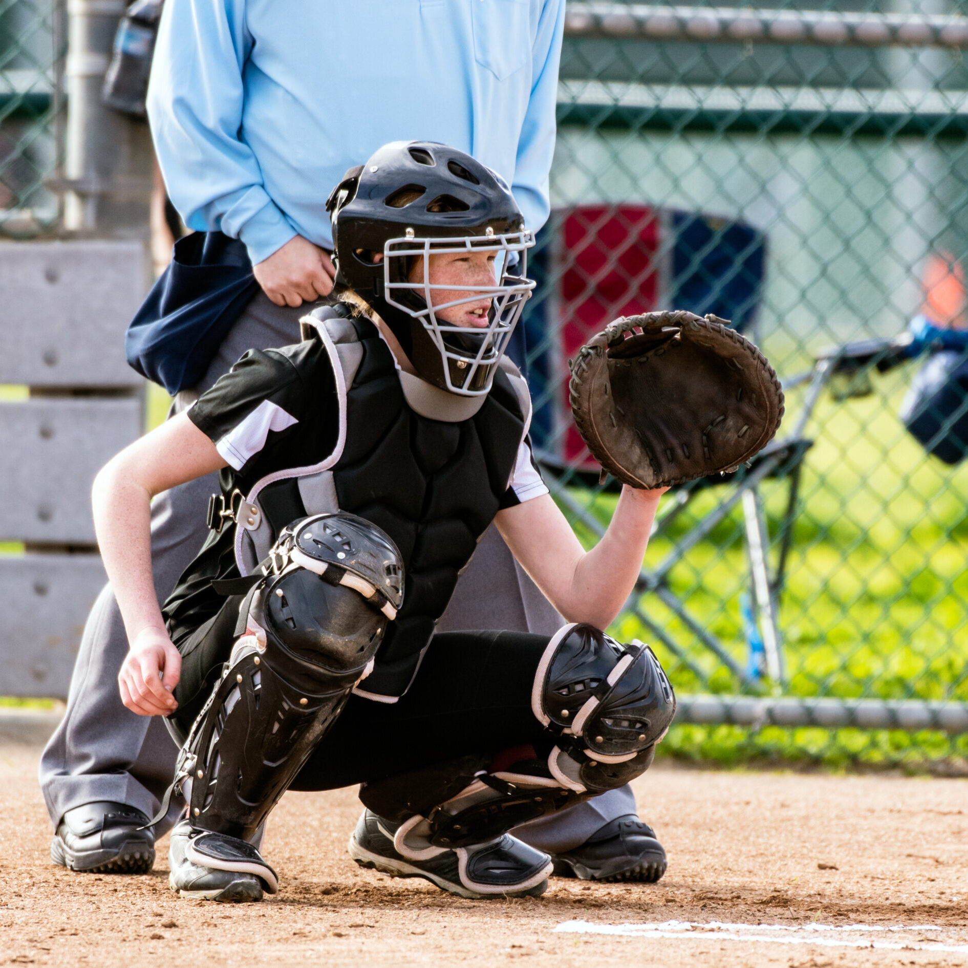 Female softball catcher in full protective gear ready to catch the first pitch.